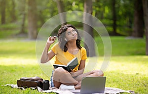 Thoughtful black girl with notebook and laptop making difficult assignment at park