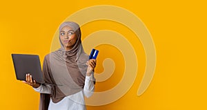 Thoughtful Black Islamic Girl In Headscarf Holding Laptop And Credit Card