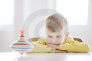 Thoughtful boy sits at the table and looks at the spinning top