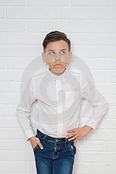 Thoughtful boy in white shirt and jeans standing against a white brick wall