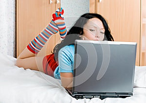 Thoughtful brunette girl with a laptop on the bed