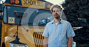 Thoughtful bus driver standing in front yellow vehicle looking camera close up.