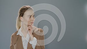 Thoughtful business woman looking at product on gray background