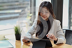 Thoughtful business woman sitting in modern office and using digital tablet.