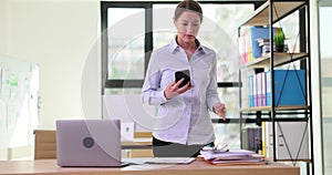 Thoughtful business woman thinking about new ideas looks at smartphone and faces desk