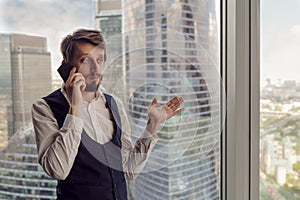 thoughtful businessman with a beard stands next to the window in the office talking