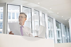 Thoughtful businessman with laptop and documents at railing