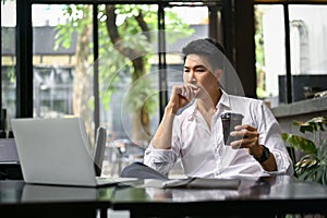 Thoughtful businessman looking at his laptop screen, remote working at a coffee shop
