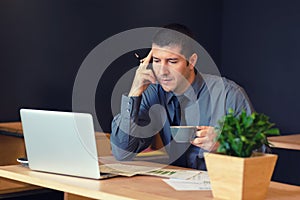 Thoughtful businessman sitting at table in trendy cafe working on laptop