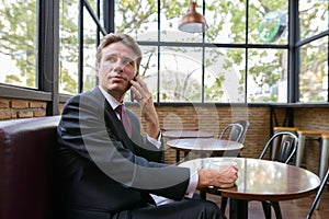 Thoughtful businessman talking on mobile phone while holding cof