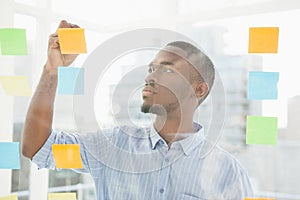 Thoughtful businessman writing on sticky notes on window