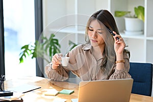 Thoughtful businesswoman holding coffee cup and reading email on computer laptop.