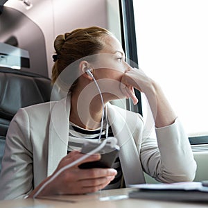 Thoughtful businesswoman listening to podcast on mobile phone while traveling by train.