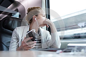Thoughtful businesswoman listening to podcast on mobile phone while traveling by train. photo