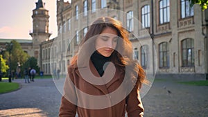 Thoughtful caucasian female is standing over ancient buildings in sunlights and enjoying good weather in fall time