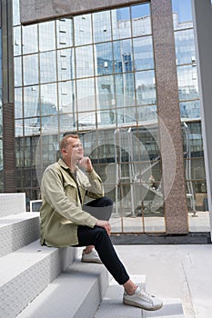 Thoughtful caucasian guy with a hearing aid sits on the stairs in the city center.