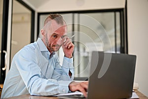 Thoughtful Caucasian male engineer looking at laptop screen, thinking and planning his work