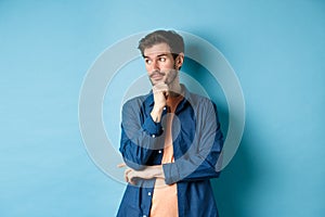 Thoughtful caucasian man looking aside at empty space and thinking, standing pensive on blue background