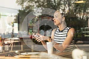 Considerado caucásico una mujer posesión móvil teléfono mientras buscando a través de café la tienda durante café romper 