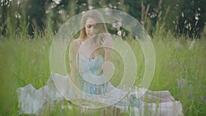 Thoughtful Caucasian woman sitting on summer meadow and picking up phone. Portrait of charming young brunette lady