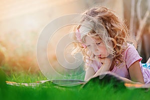 Thoughtful child girl learning and reading book on summer vacation in the garden