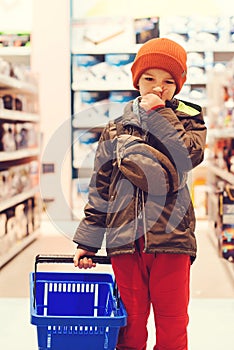 Thoughtful child holds a shopping basket in the supermarket. Itâ€™s very difficult for a boy to choose the best toy