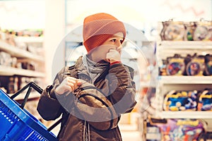 Thoughtful child holds a shopping basket in the supermarket. It is very difficult for a boy to choose the best toy. s