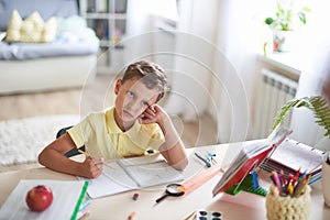 Thoughtful child sits at a table with textbooks and educational supplies.student dreams and looks to the top.scattered attention