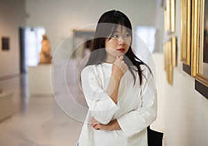 Thoughtful chinese woman standing in art museum near the painting