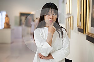 Thoughtful chinese woman standing in art museum near the painting