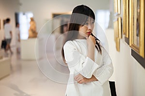 Thoughtful chinese woman standing in art museum near the painting