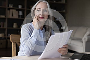 Thoughtful concerned middle aged business woman holding paper documents