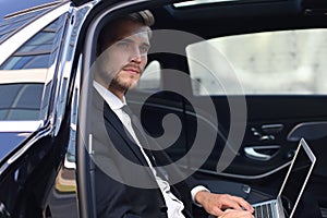 Thoughtful confident businessman sitting in the lux car and using his laptop