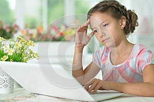 Thoughtful cute girl using laptop at home