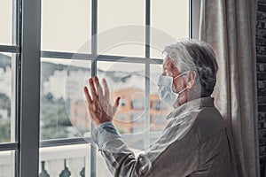 Thoughtful depressed old man looking out of window with hope, thinking over business lockdown loss, future vision after epidemic
