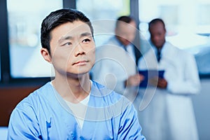Thoughtful doctor in medical uniform with collegues behind in clinic