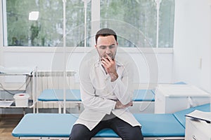 Thoughtful doctor sitting in a operating room with his hand on head