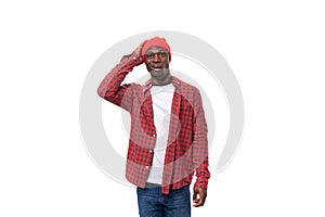 thoughtful doubting young american man in red cap and plaid shirt scratching his head on white background with copy