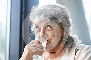 Thoughtful elderly woman drinks water