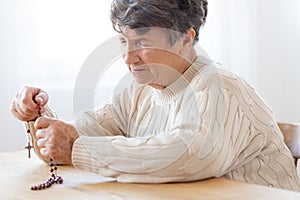 Thoughtful elderly woman praying to god while holding a red rosa