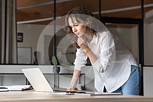 Thoughtful engaged young manager woman using laptop at workplace