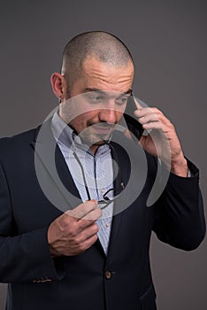 Thoughtful entrepreneur talking on mobile phone while keeping his spectacles rim at his chin