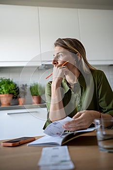 Thoughtful female analysing budget, verifying income and expenses, thinking while looking at window