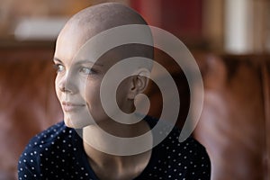 Thoughtful female cancer patient sitting on couch looking aside pondering