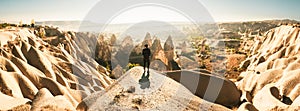 Thoughtful Female person stand look over dramatic valley on hazy morning sunrise with fairy chimneys background. Solo exploration
