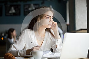 Thoughtful female writer or student writing notes in coffee shop