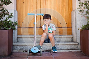 Thoughtful five year old boy with his scooter outdoors