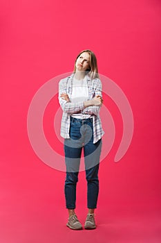 Thoughtful frowning young woman standing and thinking over pink background