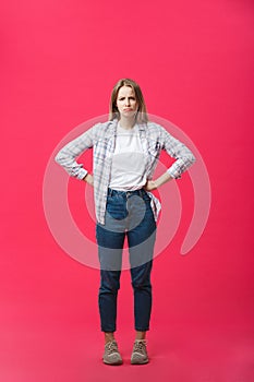 Thoughtful frowning young woman standing and thinking over pink background