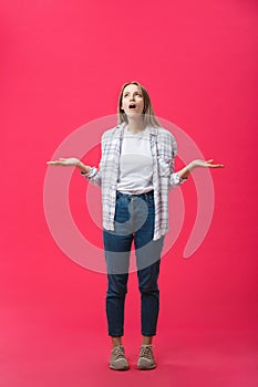 Thoughtful frowning young woman standing and thinking over pink background